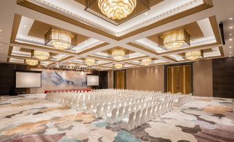 a large conference room with multiple rows of chairs arranged in a symmetrical fashion , under a high ceiling with chandeliers at Sanya Xizang Hotel