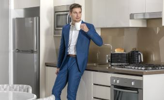 a man in a blue suit is standing in a kitchen , holding a cup of coffee at Meriton Suites North Ryde