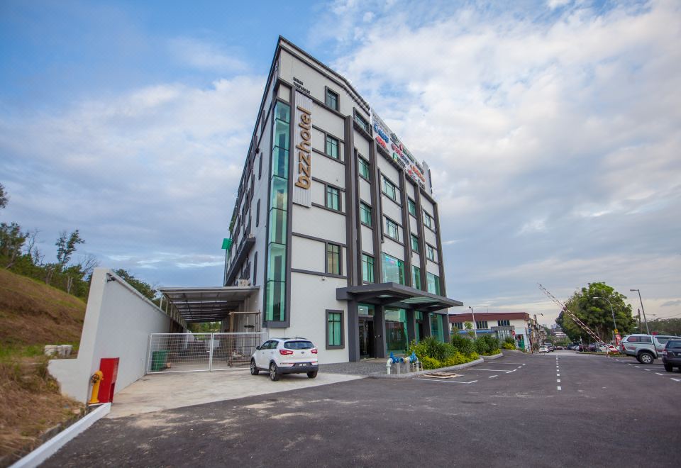 a modern , white building with green and red accents , surrounded by trees and a parking lot at Bzz Hotel Skudai