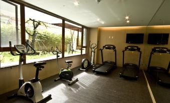 a well - lit indoor gym with various exercise equipment , including treadmills and stationary bikes , near large windows that offer views of the outdoors at Alishan House