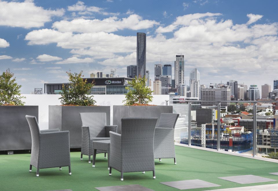 a rooftop patio with a view of the city skyline , where several chairs and a table are arranged for outdoor dining at Direct Collective - Pavilion and Governor on Brookes