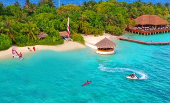 a tropical island with palm trees , a thatched roof hut , and clear blue water with people kayaking at Eriyadu Island Resort