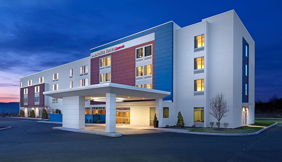 a large , modern hotel building with multiple stories and a red roof , situated in front of a clear blue sky at dusk at SpringHill Suites Dayton Vandalia