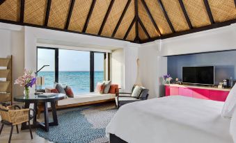 a modern , minimalist bedroom with a large window offering a view of the ocean and a comfortable living area at Four Seasons Resort Maldives at Kuda Huraa