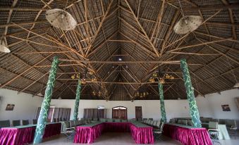 a large , empty room with high ceilings and thatched roofs has two round tables with red tablecloths at AA Lodge Amboseli