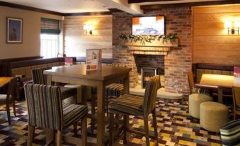 a cozy living room with a brick fireplace and a dining table , where several chairs are arranged around it at Premier Inn Grantham