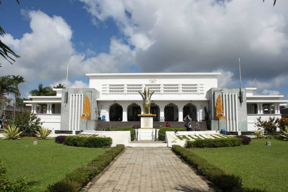 a large white building surrounded by grass and trees , with a statue in the front at Grand Elty Singgasana Hotel
