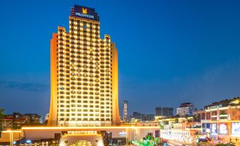 a tall hotel building with a neon sign on the side is illuminated at night at Millennium Harbourview Hotel Xiamen