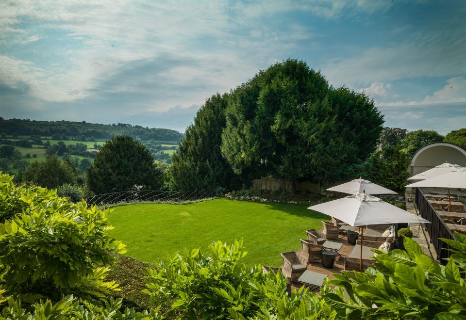 a large grassy field with a wooden deck and an umbrella in the foreground , surrounded by trees at The Painswick
