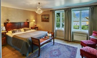 a large bed with a wooden headboard is in a room with a chandelier , chairs , and a window at Fretheim Hotel