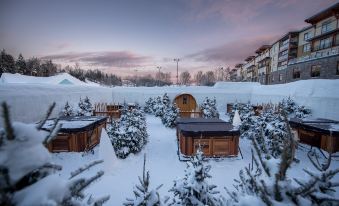a snowy landscape with multiple wooden cabins and a building in the background , under a pink sky at Hôtel de Glace