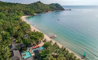 a beautiful beach resort with a large white building , surrounded by lush green trees and a clear blue ocean at Anantara Rasananda Koh Phangan Villas
