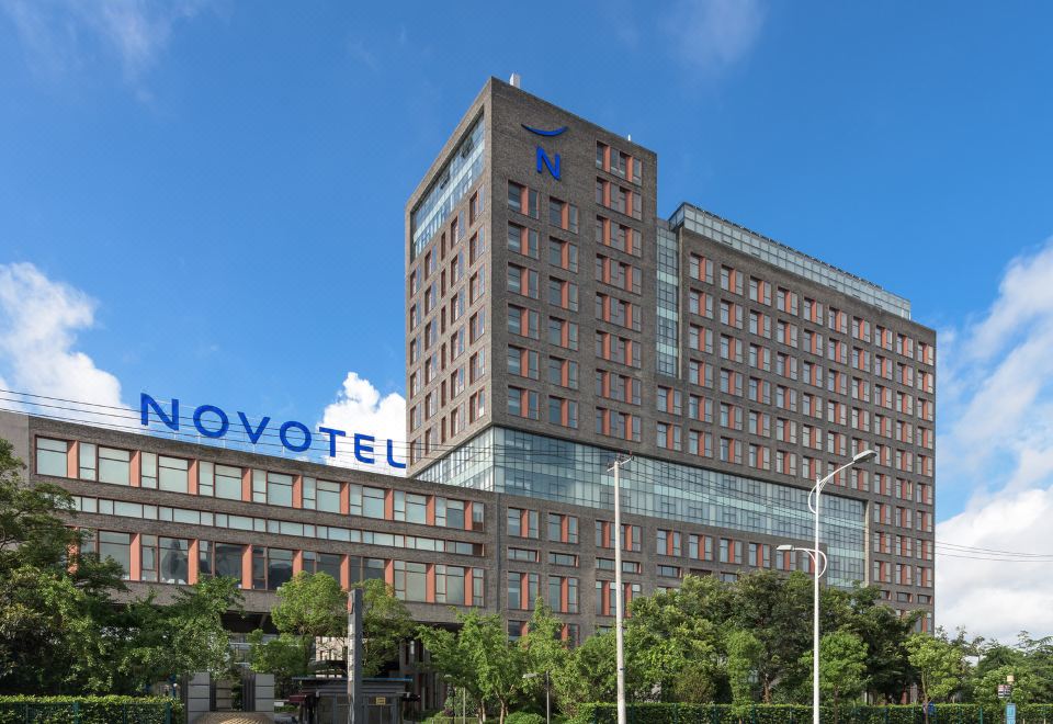 The exterior view from across the street includes an office building in front and another hotel at Novotel Shanghai Clover