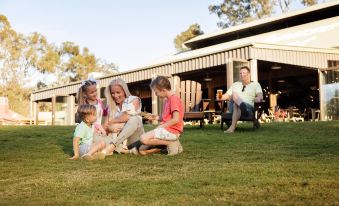 a family of four , consisting of a man , a woman , and two children , is sitting on the grass in front of a building , at Paradise Country Farmstay