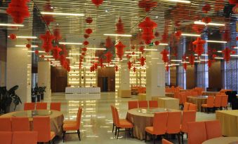 a large banquet hall with multiple tables and chairs , orange tablecloths , and red lanterns hanging from the ceiling at Spring Hotel