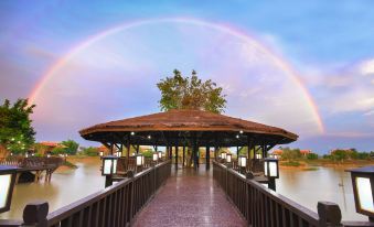 a beautiful rainbow is visible in the sky over a wooden bridge with a thatched roof pavilion at Mane Hariharalaya