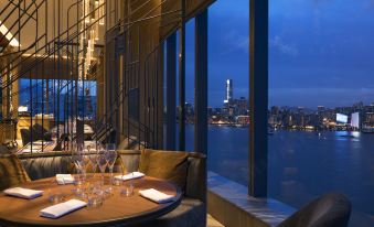 A restaurant with large windows that offer a view of the city and tables positioned in front, all facing outward at Hyatt Centric Victoria Harbour Hong Kong