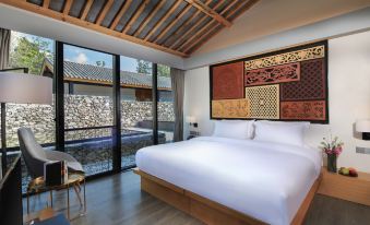 a large bed with white linens is in a room with a sliding glass door that leads to an outdoor area at The Rock Hotel
