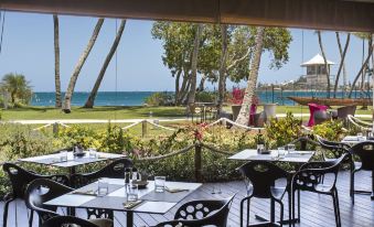 an outdoor dining area with tables and chairs set up for a meal , overlooking the ocean at Chateau Royal Beach Resort & Spa, Noumea