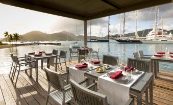 an outdoor dining area overlooking a body of water , with tables and chairs arranged for guests at South Point Antigua