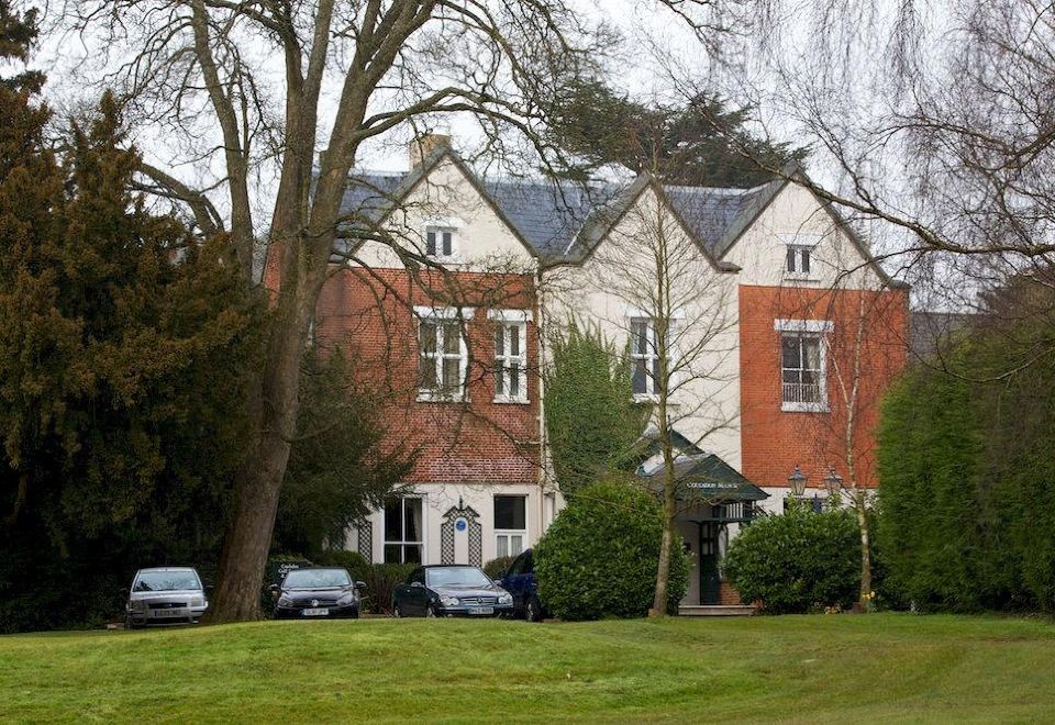a large , two - story brick house with white trim and a green lawn in front of it at Coulsdon Manor Hotel and Golf Club