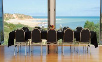 a long table with chairs is set up in a room with a view of the ocean at Eco Beach Wilderness Retreat