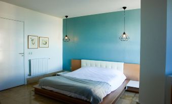 a modern bedroom with a white bed , blue walls , and two hanging lights above the bed at The View Gammarth