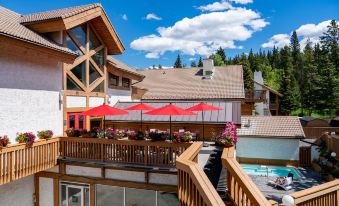 a wooden deck with multiple chairs and tables , as well as a pool and umbrellas at Banff Rocky Mountain Resort