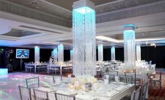 a large , white banquet hall with multiple tables and chairs , each table set for a banquet , and a tall cylindrical light display at Westminster Hotel