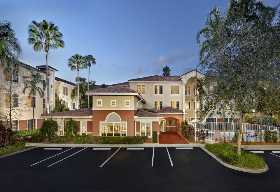 a modern apartment building with multiple parking spaces , surrounded by palm trees and a clear blue sky at Residence Inn Fort Lauderdale Weston