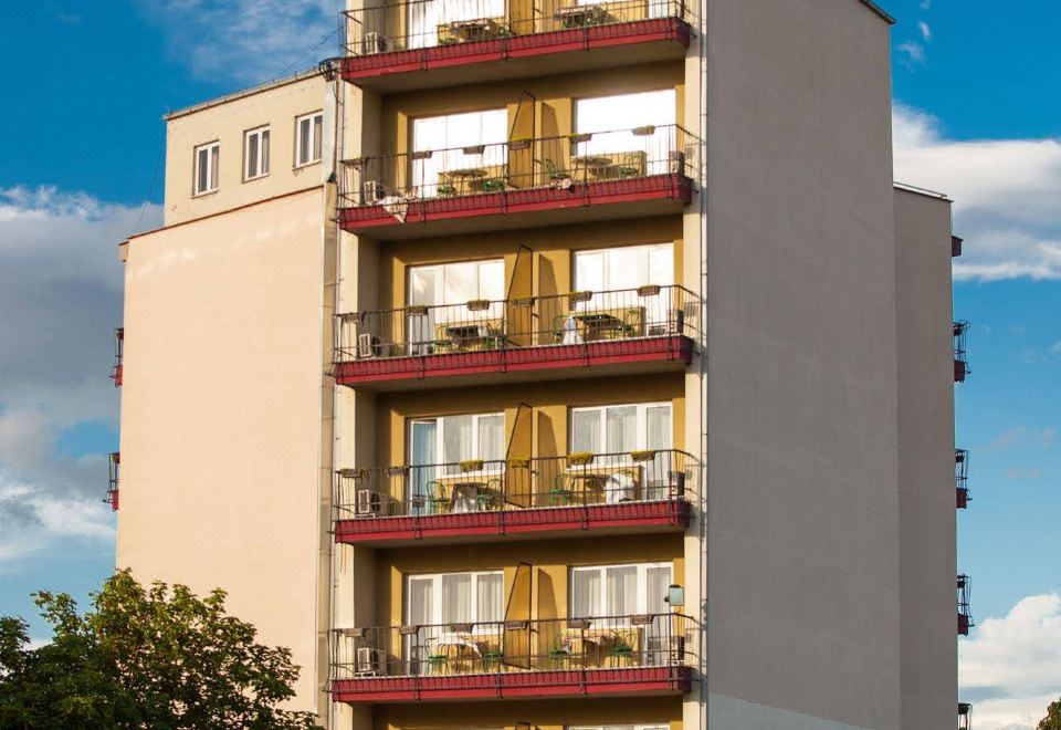 a tall , beige building with red accents and balconies , surrounded by trees and blue skies at Hotel Bellevue