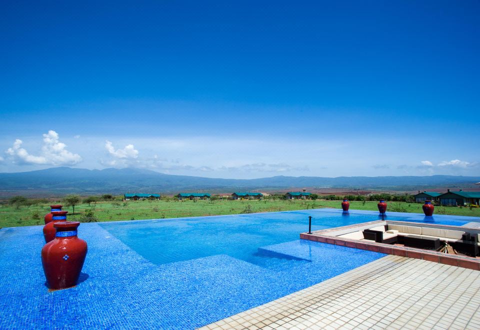 a large swimming pool with a beautiful blue water and surrounding mountains in the background at Ngorongoro Oldeani Mountain Lodge
