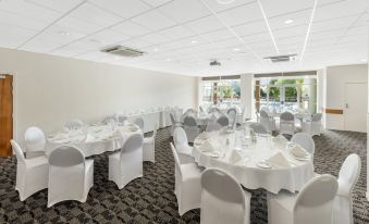 a large dining room with white tables and chairs set up for a formal event , possibly a wedding reception at Rydges Rotorua, an EVT Hotel