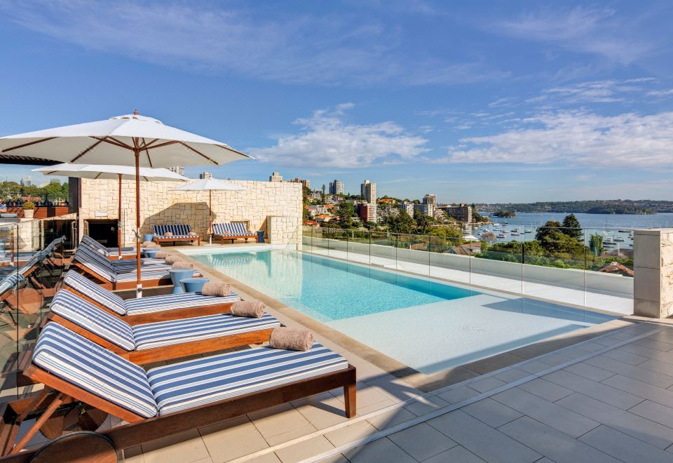 a large outdoor pool surrounded by lounge chairs and umbrellas , with a city skyline visible in the background at InterContinental Sydney Double Bay, an IHG Hotel