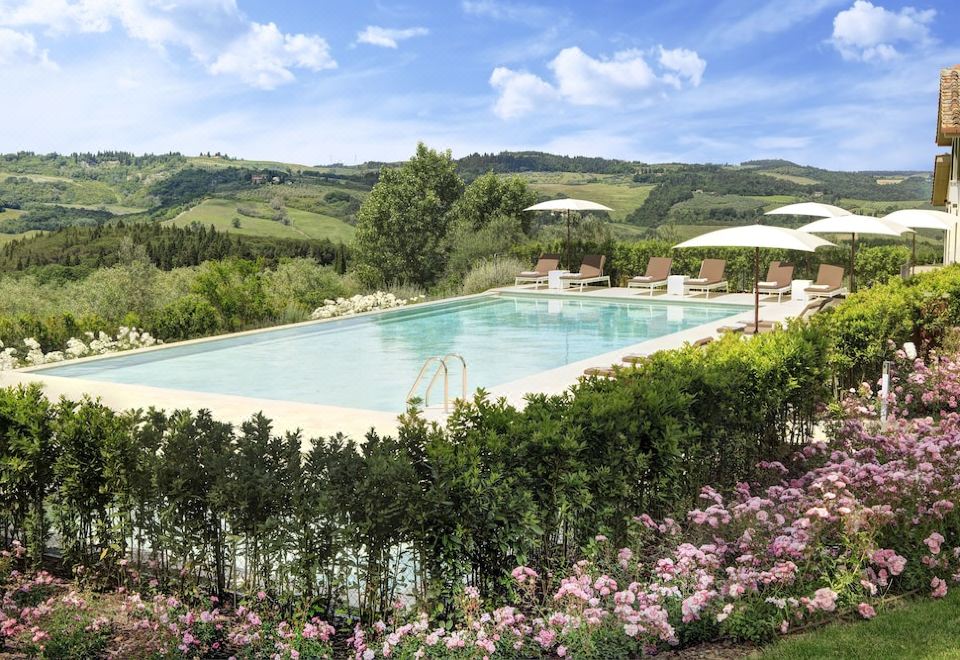 a large swimming pool surrounded by lush greenery and flowers , with umbrellas and lounge chairs placed around the pool area at Villa le Calvane