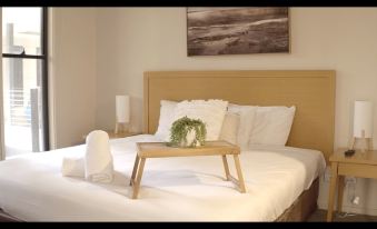 a bed with a wooden tray on it , surrounded by white linens and a lamp at Barwon Heads Resort