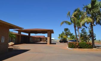 a building with a covered entrance and palm trees in the foreground , under a clear blue sky at The Lodge Motel