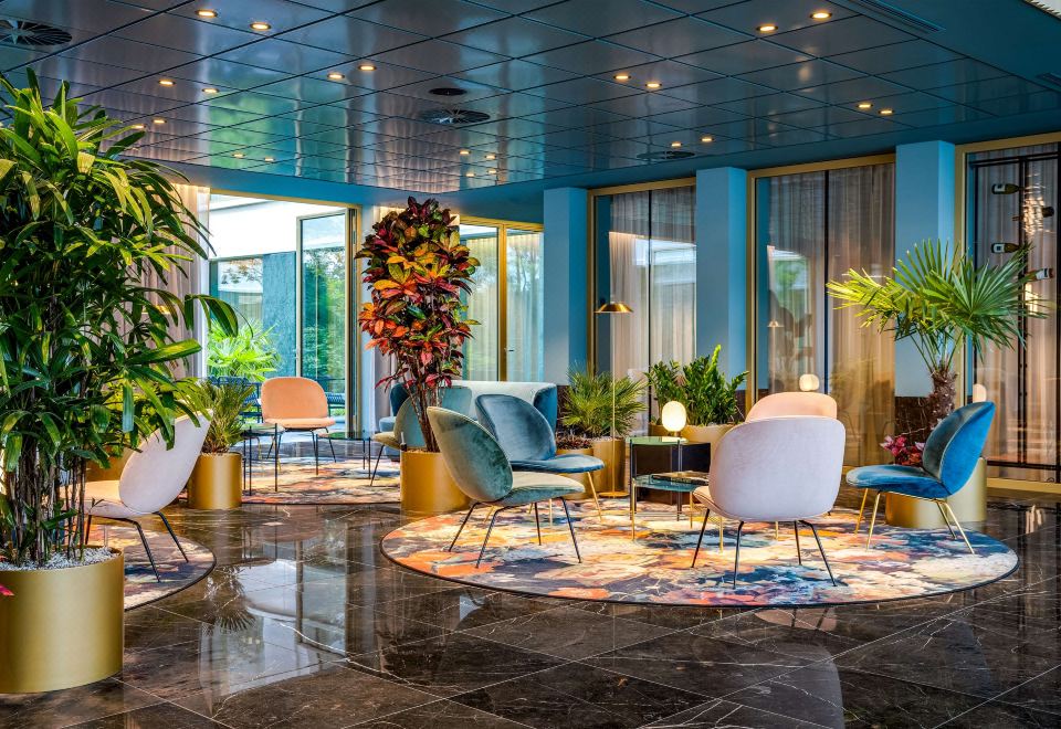 a modern lounge area with blue walls , wooden floors , and various furniture pieces , including chairs , tables , and potted plants at NH Collection Antwerp Centre