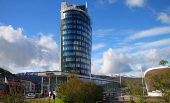 a tall , modern building with a circular design is surrounded by trees and other buildings at Scandic Narvik