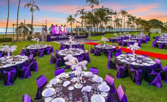 a large outdoor event space with purple tablecloths , white plates , and wine glasses on tables , set up for an event at Mindil Beach Casino Resort