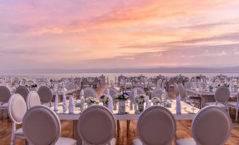a large outdoor dining area with white tables and chairs set up for a formal event , overlooking the ocean at Kempinski Hotel Ishtar Dead Sea