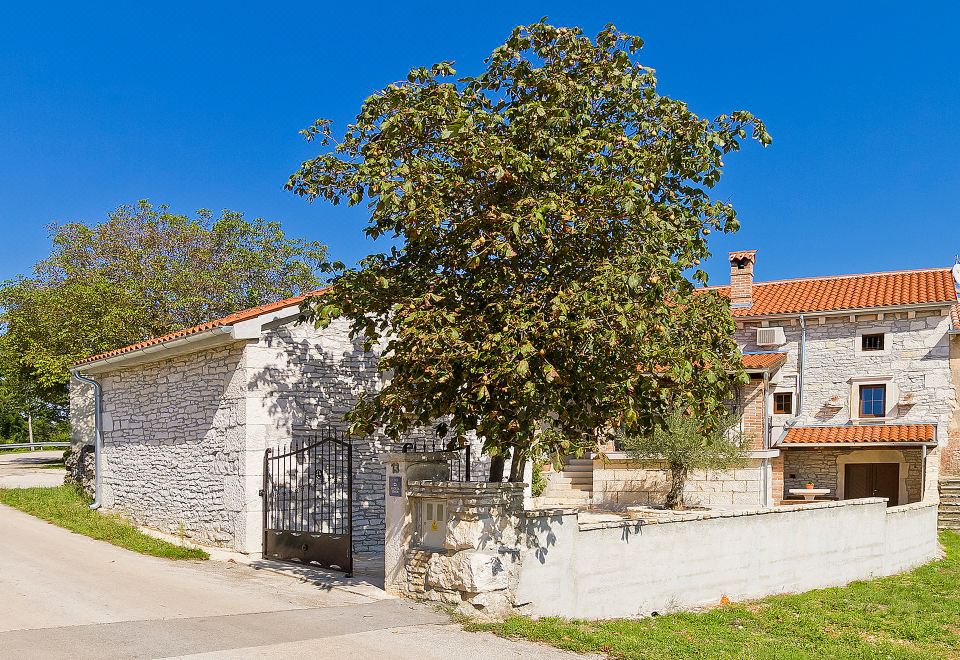 a house with a large tree in front of it , situated next to a brick wall at Mila