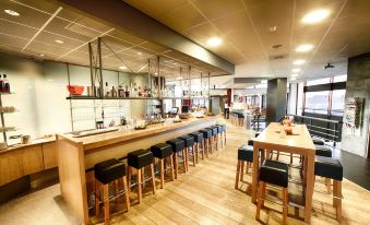 a modern restaurant with wooden tables and chairs , a long bar , and an open kitchen at Leonardo Hotel Lelystad City Center