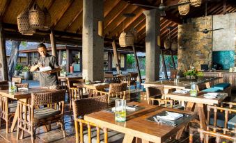 a man is standing at the end of an open - air dining area with wooden tables and chairs at Jeeva Klui Resort