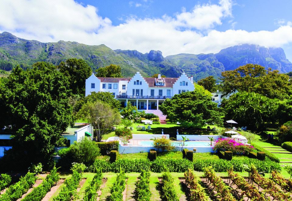 a large white house surrounded by a lush green garden , with mountains in the background at The Cellars-Hohenort