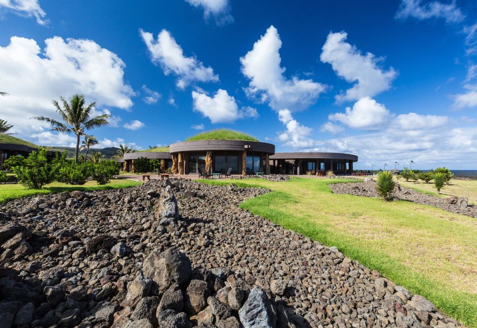 a large , modern house with a green dome is surrounded by rocks and palm trees at Nayara Hangaroa