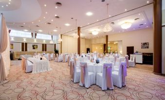 a large banquet hall with white and purple decorations , including chairs , tables , and chandeliers , set up for an event at Hotel Boss