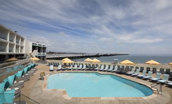 a large outdoor pool surrounded by lounge chairs and umbrellas , with a pier in the background at Dream Inn Santa Cruz