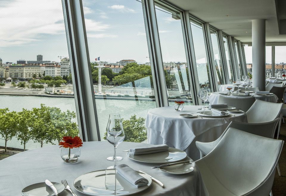 a restaurant with a view of the water , featuring elegant dining tables and chairs set for a meal at Sofitel Lyon Bellecour