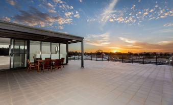 a large , open - air terrace with a glass roof and wooden furniture , overlooking a beautiful sunset over a distant cityscape at The Penthouse
